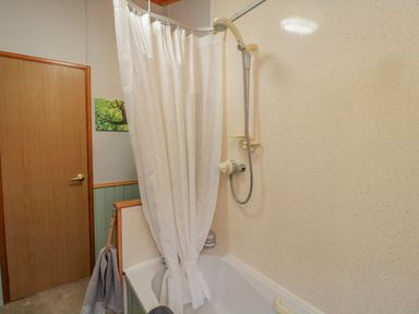 A bathroom with a bathtub and shower with a white curtain and a wooden door at 4 The Oaks in Swarland