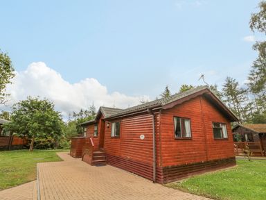 A wooden cabin house with paved walkway and surrounding grass at 4 The Oaks in Swarland