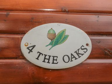 An oval sign with an acorn and leaves and the text 4 The Oaks on a wooden wall at 4 The Oaks in Swarland