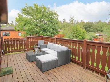 An outdoor wooden deck with a wicker sofa set and a table with glasses and a bottle at 4 The Oaks in Swarland