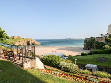 A garden with a wooden bench and flowerbed overlooking a sandy beach and sea at Ty Cwtch in Tenby