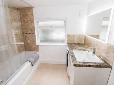 A bathroom with a bathtub with a shower curtain a sink with a marble countertop and a washing machine under the counter at Ty Cwtch in Tenby