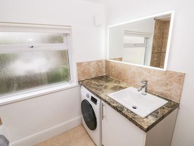 A bathroom with a washing machine under a marble countertop with a sink and a lighted mirror at Ty Cwtch in Tenby