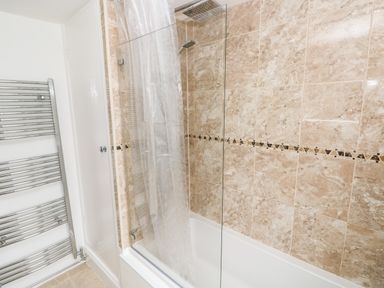 A bathroom with a bathtub shower combo with glass and curtain and tiled walls and a chrome heated towel rail at Ty Cwtch in Tenby