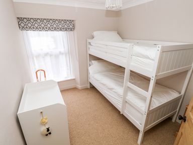 A small bedroom with white bunk beds a window with patterned blind and a white changing table at Ty Cwtch in Tenby