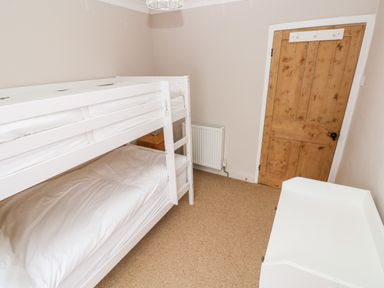 A bedroom with white bunk beds a wooden door a white dresser and a small bedside table at Ty Cwtch in Tenby