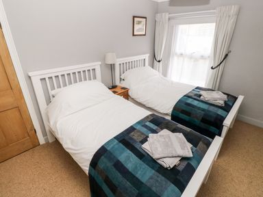 A bedroom with two single beds side by side with white headboards blue checkered blankets and folded towels at Ty Cwtch in Tenby