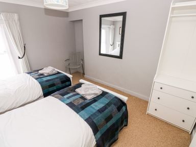 A bedroom with two single beds towels on beds a metal chair a wall mirror and white dresser at Ty Cwtch in Tenby