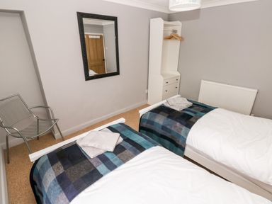 A bedroom with two single beds, a metal chair, a wall mirror, and a white wardrobe at Ty Cwtch in Tenby