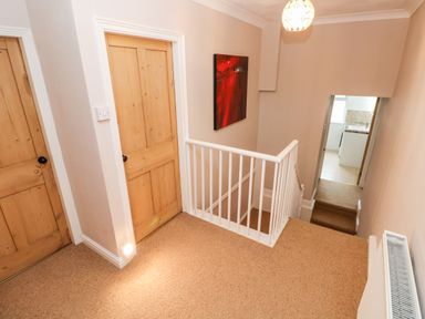 A hallway with two wooden doors a white railing and carpeted stairs leading to a tiled floor at Ty Cwtch in Tenby