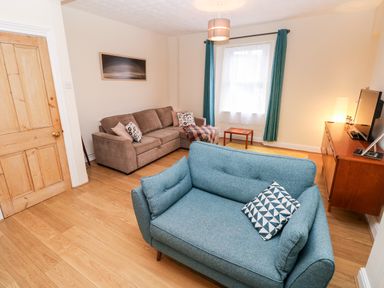 A living room with two sofas a wooden door a small table a television on a wooden cabinet and curtains at Ty Cwtch in Tenby