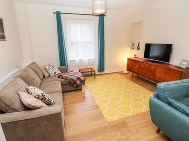 A living room with a brown sofa blue armchair yellow rug and wooden TV console at Ty Cwtch in Tenby