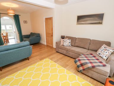 A living room with a beige sofa and blue armchairs a yellow patterned rug and a painting on the wall at Ty Cwtch in Tenby