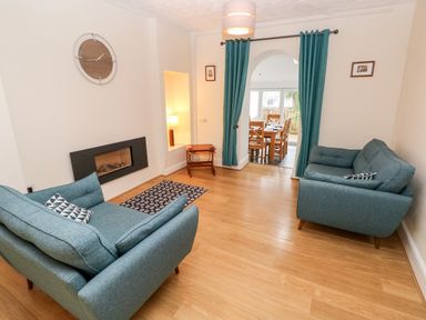 A living room with two blue sofas a wall clock a fireplace and an archway leading to a dining area at Ty Cwtch in Tenby