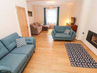 A living room with two blue sofas and a beige sofa near a window with blue curtains at Ty Cwtch in Tenby