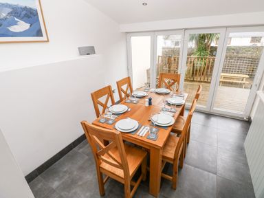 A dining room with a wooden table set for six near glass doors opening to a wooden deck at Ty Cwtch in Tenby