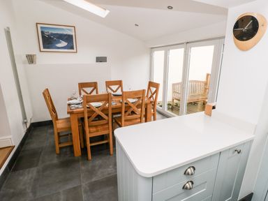 A dining area with wooden table and chairs set for six next to glass doors with a wooden bench outside at Ty Cwtch in Tenby