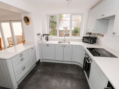 A kitchen with light blue cabinets, a sink under a window, a microwave, a stove, and a kettle at Ty Cwtch in Tenby