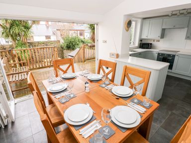 A dining area with a wooden table set for six and a kitchen with cabinets and appliances at Ty Cwtch in Tenby