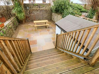 A stone patio with a wooden picnic table and stairs leading down to it at Ty Cwtch in Tenby