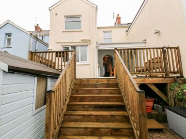 Wooden stairs leading to a back entrance of a pale yellow house with a deck and a shed to the side at Ty Cwtch in Tenby