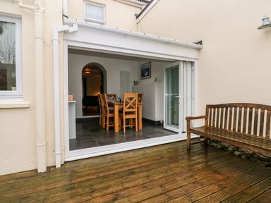 An outdoor wooden bench on a deck in front of a sliding glass door opening to a dining area with a wooden table and chairs at Ty Cwtch in Tenby