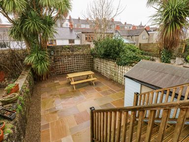 A paved backyard with a wooden picnic table a small shed and wooden stairs at Ty Cwtch in Tenby