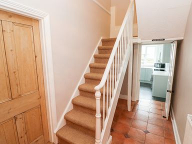 A hallway with carpeted stairs and a wooden door leading to a kitchen at Ty Cwtch in Tenby