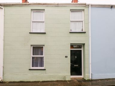 A pale green house facade with three windows and a black front door numbered 6 at Ty Cwtch in Tenby