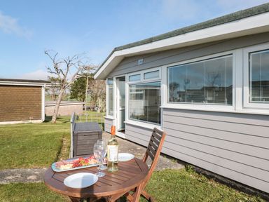 An outdoor patio area with a wooden table and chair set with wine glasses a bottle of wine and a platter of snacks next to a grey building at Wagtails Norton near Dartmouth