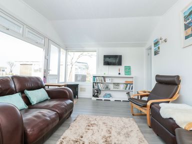 A living room with brown leather sofa and chair a bookshelf and TV at Wagtails in Norton near Dartmouth