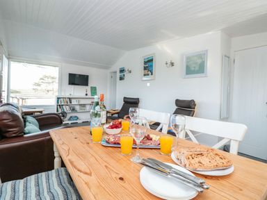A dining table with food and drinks in a living room with chairs bookshelves and a wall mounted tv at Wagtails in Norton near Dartmouth