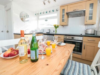 A kitchen with wooden cabinets a table set with fruit wine glasses and juice at Wagtails in Norton near Dartmouth