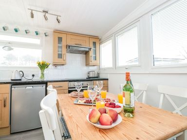 A kitchen with a wooden dining table set with fruit plates glasses orange juice and a bottle at Wagtails in Norton near Dartmouth