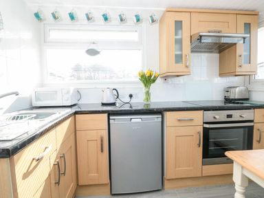 A kitchen with wooden cabinets a microwave kettle toaster oven and a vase with flowers on the counter at Wagtails in Norton near Dartmouth