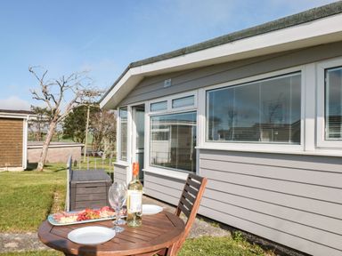 A wooden outdoor table with wine bottle glasses and a plate of food outside a grey building with windows at Wagtails Norton near Dartmouth