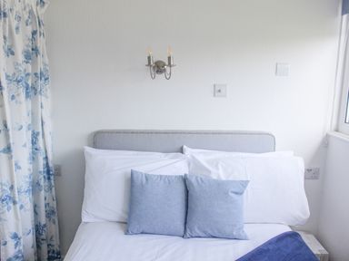 A bed with white and blue pillows and floral curtains in a bedroom at Wagtails Norton near Dartmouth