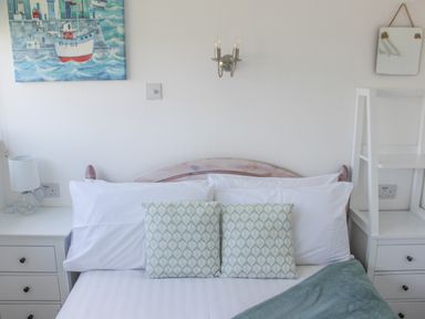 A bedroom with a bed with patterned cushions a bedside table with a lamp and a painting of a boat at Wagtails Norton near Dartmouth