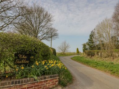 A country road with daffodils and a sign that says The Stables at The Stables in Belbroughton