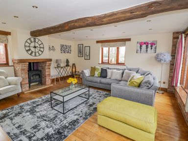 A living room with a grey sofa a yellow ottoman a brick fireplace and large wall clock at The Stables in Belbroughton