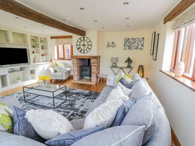 A living room with a gray sofa and cushions a glass coffee table a fireplace and a television at The Stables in Belbroughton