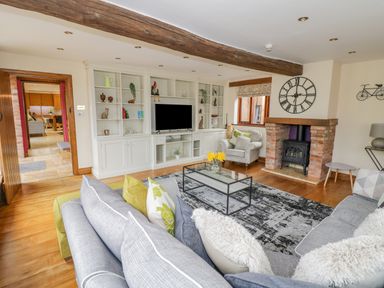 A living room with a gray sofa and armchair a fireplace and built in shelves with a television at The Stables in Belbroughton