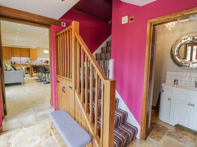 A hallway with stairs and a bench next to a bathroom and an open kitchen living area at The Stables in Belbroughton