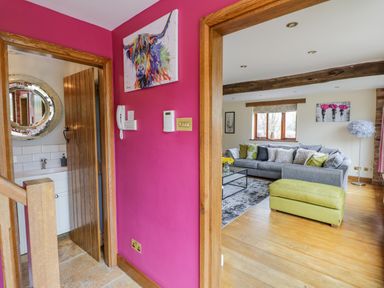 A hallway with magenta walls leading to a living room with grey sofas and green ottoman at The Stables in Belbroughton
