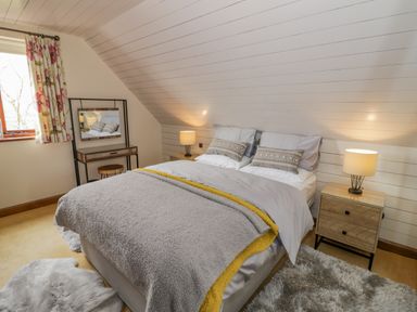 A bedroom with a double bed bedside tables lamps a vanity table and floral curtains at The Stables in Belbroughton