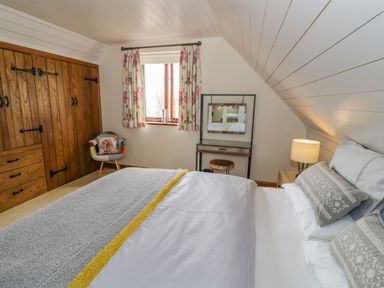 A bedroom with a bed side table lamp wooden wardrobe patterned curtains chair and vanity table at The Stables in Belbroughton