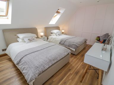 A bedroom with two beds bedside tables with lamps a desk and a chair at The Stables in Belbroughton