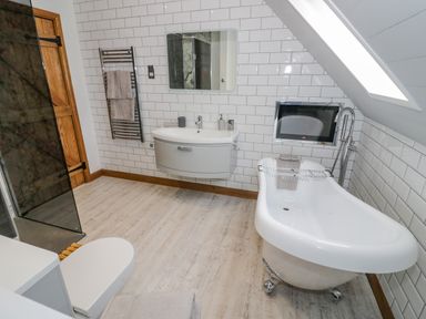 A bathroom with a freestanding bathtub toilet sink mirror towel rack and skylight at The Stables Belbroughton