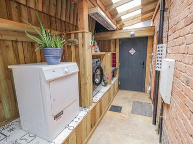 A laundry room with a washing machine and dryer on tiled shelves and a wooden door at The Stables in Belbroughton