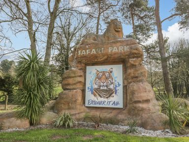 An outdoor entrance sign for a safari park with a lion statue and a tiger image surrounded by trees and plants